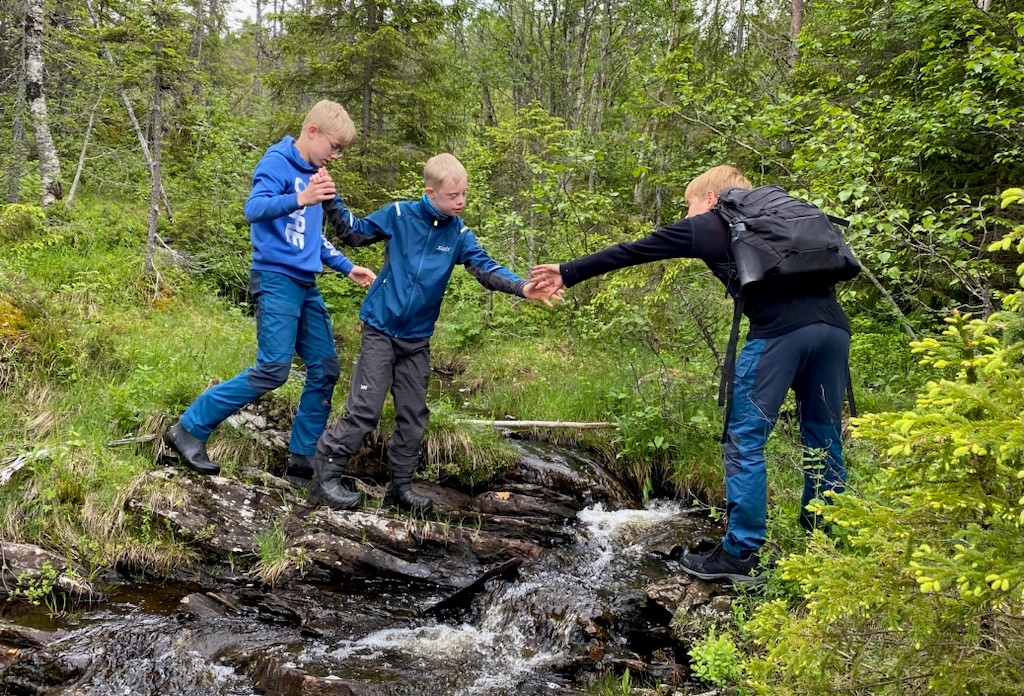 Tre gutter hjelper hverandre med å krysse en bekk